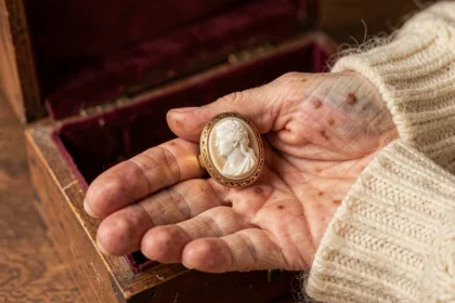 Bague camée ancienne en or sur la paume d'une femme âgée, posée sur un écrin en velours bordeaux