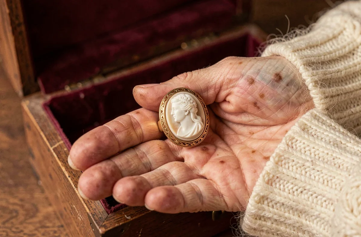 Bague camée ancienne en or sur la paume d'une femme âgée, posée sur un écrin en velours bordeaux
